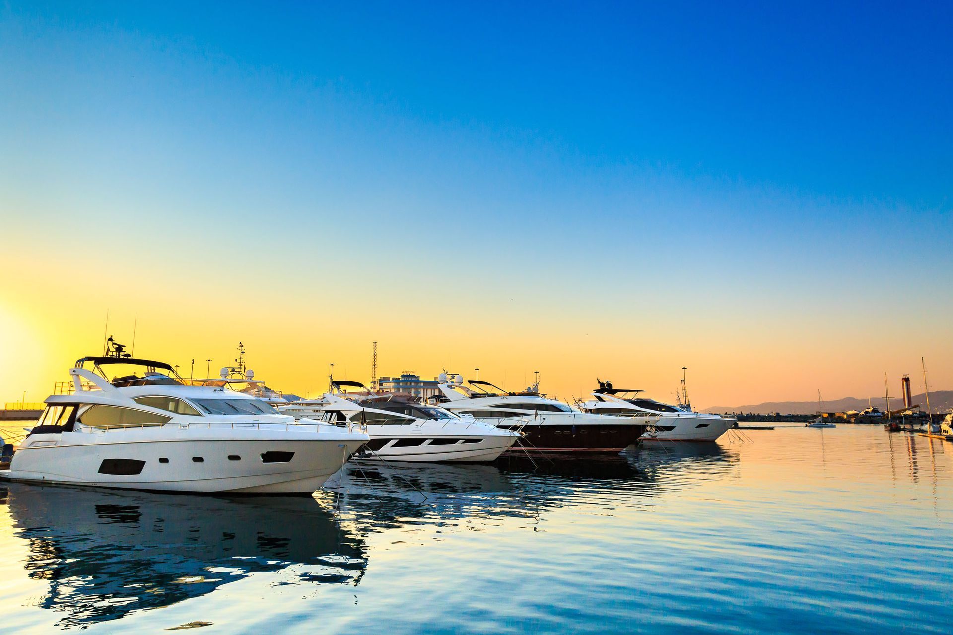 Yachts docked at a marina during sunset with a colorful sky and calm water.