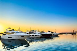 Yachts docked at a marina during sunset with a colorful sky and calm water.