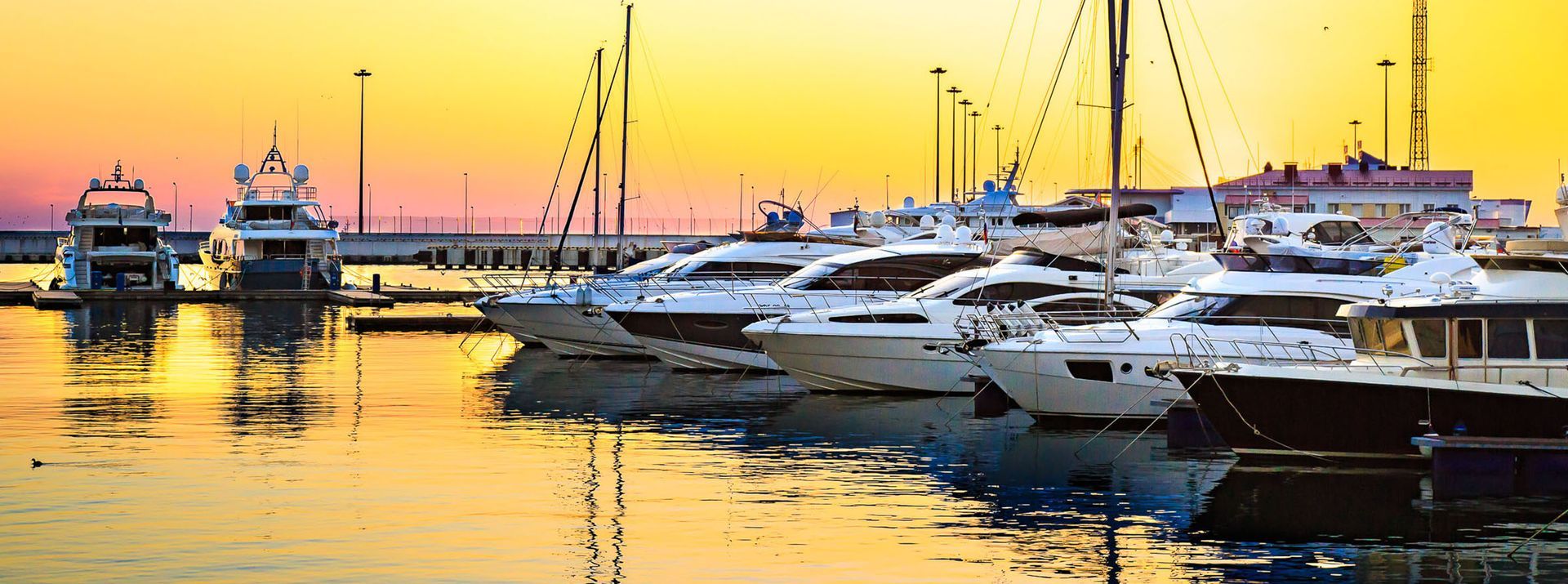 Boats docked in a harbor at sunset, with golden and orange sky reflecting in the water.