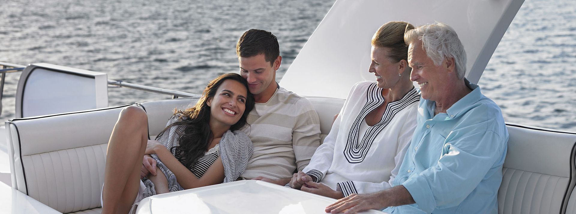 A family relaxes on a boat. They are sitting together, smiling, with the ocean in the background.