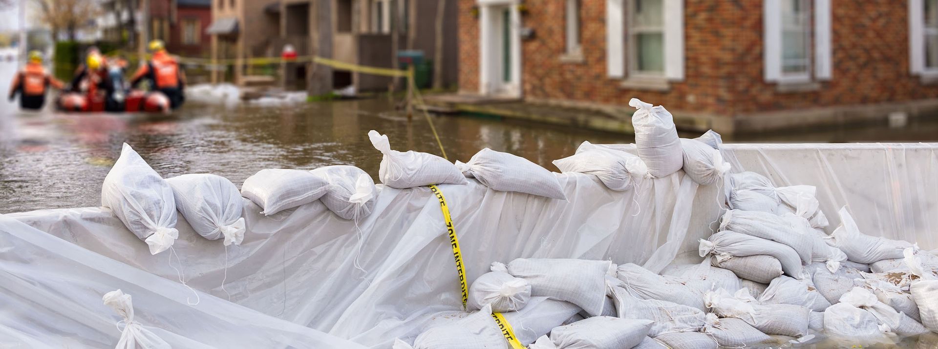 Sandbags barricade a flooded street. Rescue workers in orange life vests navigate the water in a raft.
