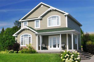 Two-story house with green siding, white trim, porch, and a green roof against a blue sky.