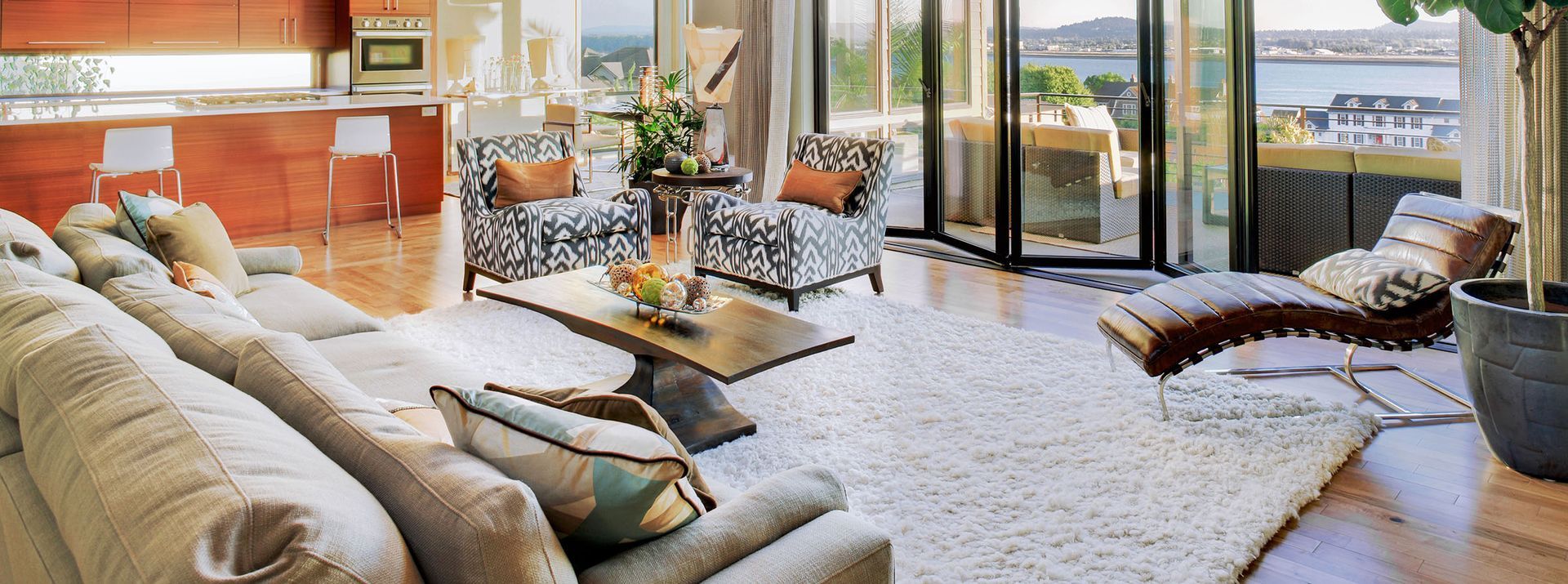 Living room with a large white rug, sectional sofa, patterned armchairs, and a chaise lounge with a view of the water.
