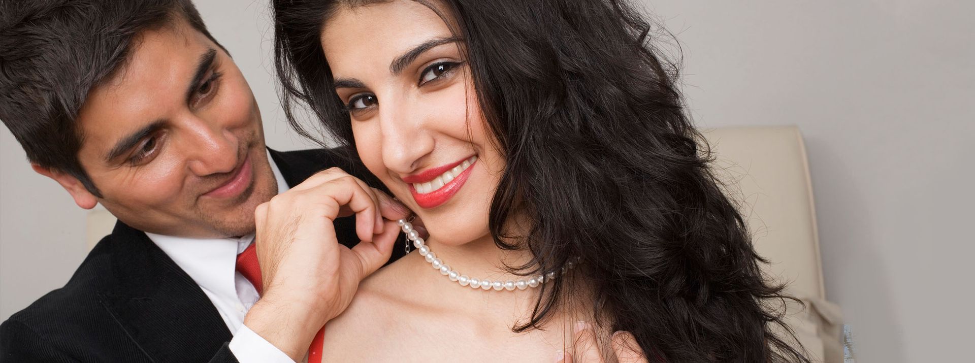 Man putting a pearl necklace on a smiling woman.