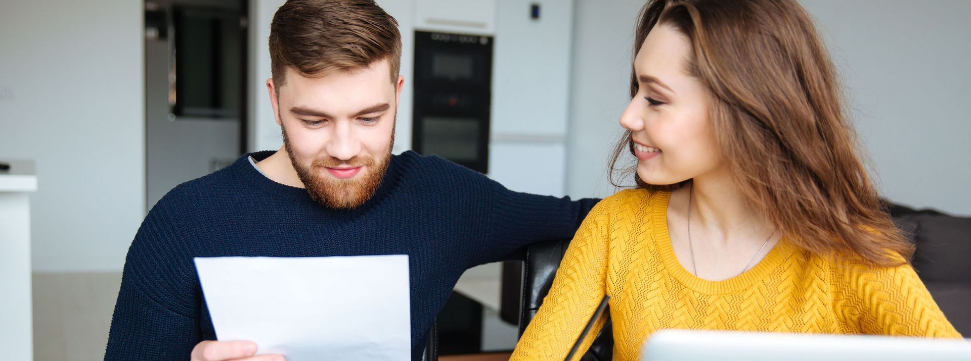 A couple reviews paperwork together at a table. The woman smiles, and the man reads a document.