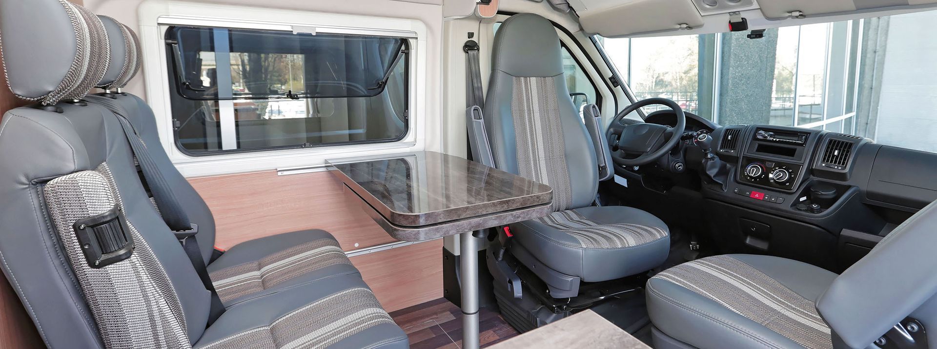 Interior of a camper van with seats, table, and dashboard.