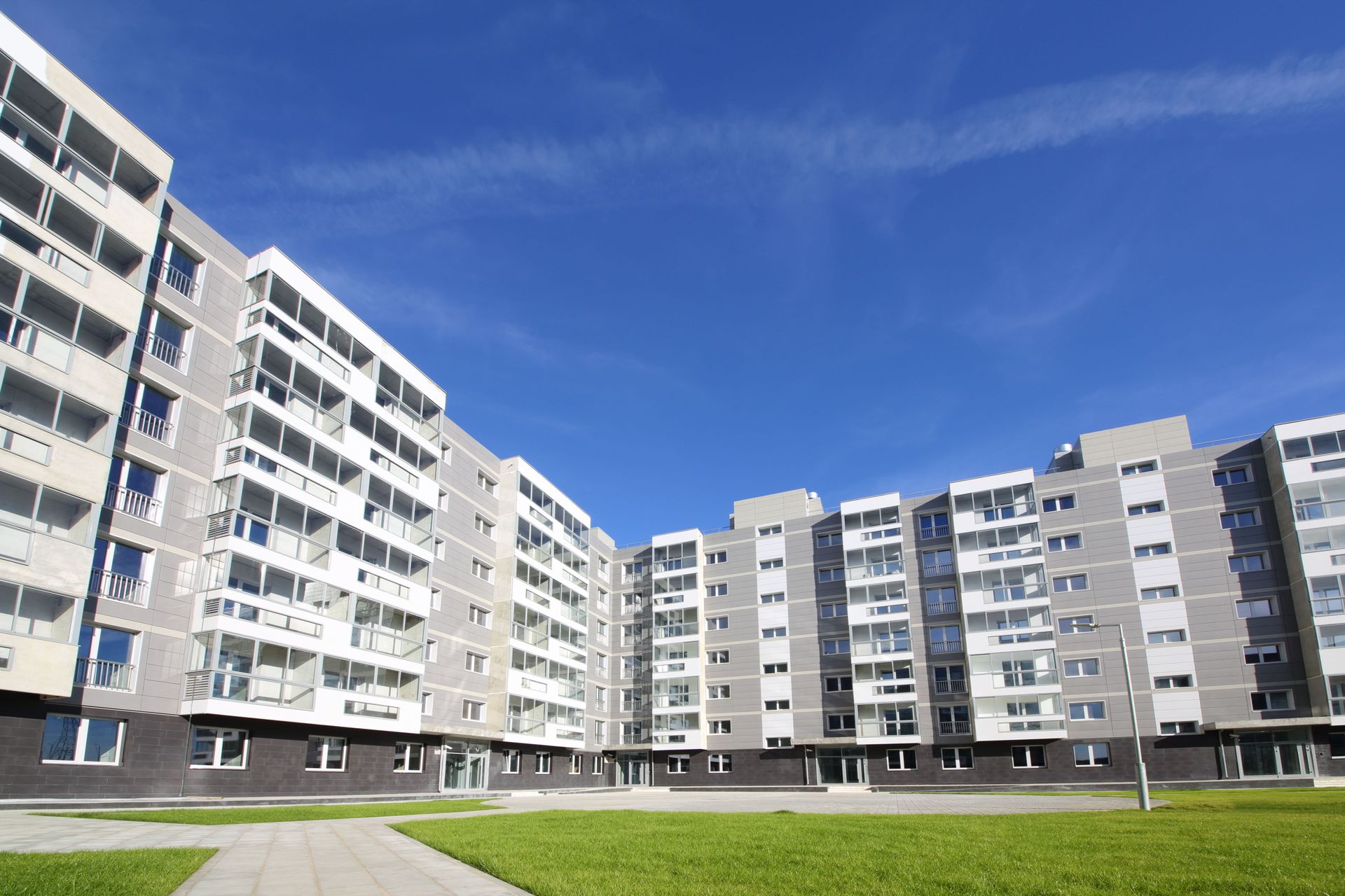Multi-story gray apartment building with balconies, under a blue sky.