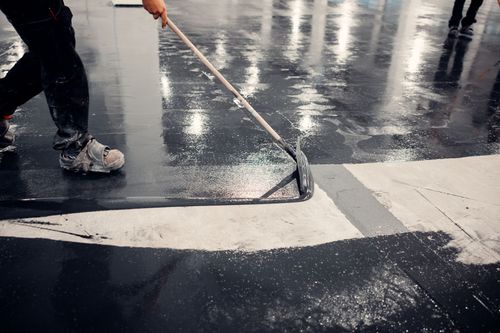 Worker painting white road markings on a wet street with a long-handled roller