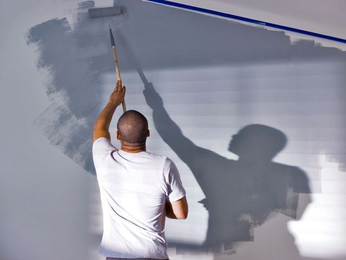 Person painting a light gray wall with a roller, casting a shadow on the surface.