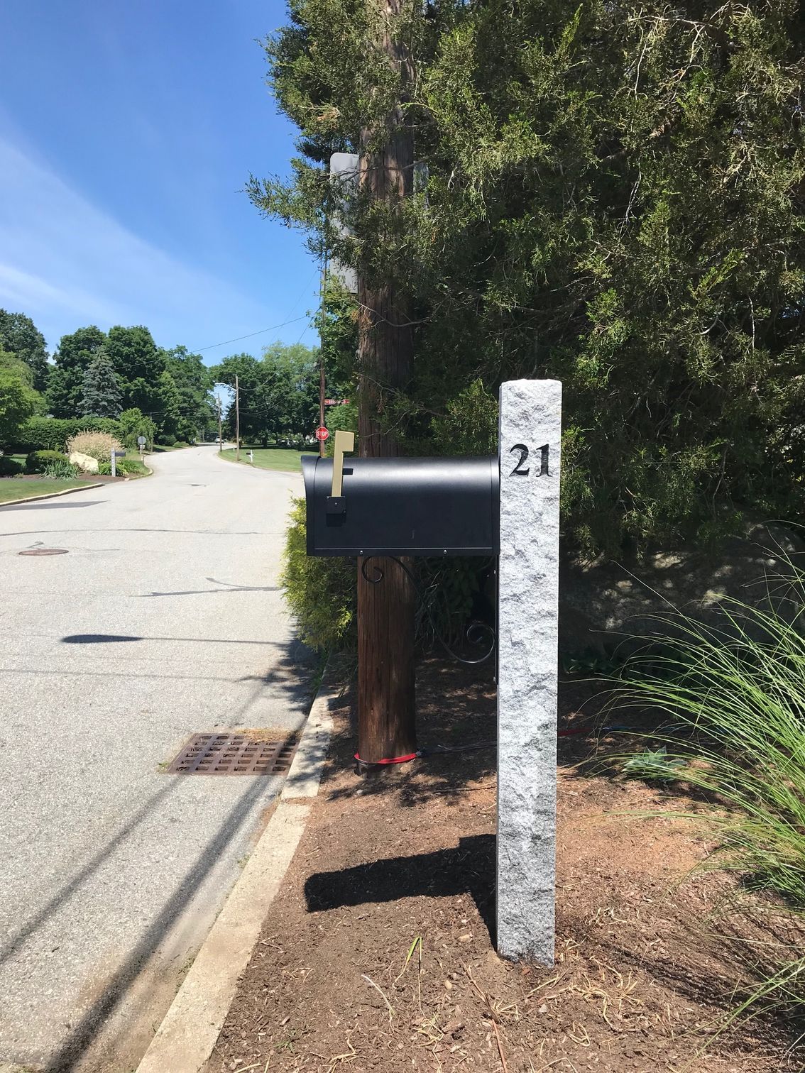 A black mailbox mounted on a tall, gray granite post labeled 
