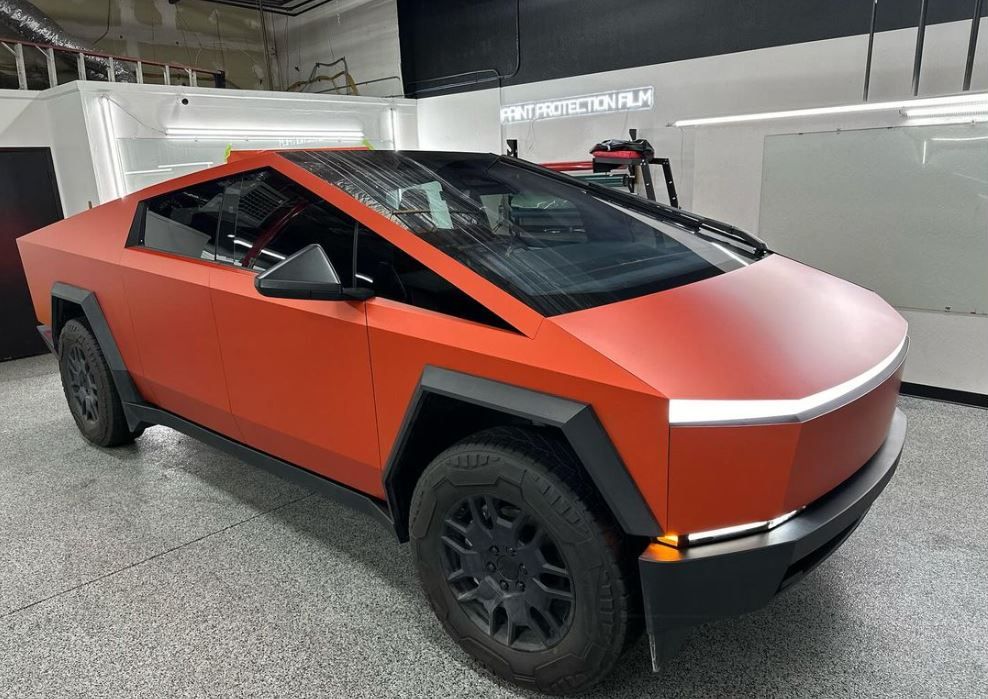 An orange Tesla cybertruck is parked in a garage.