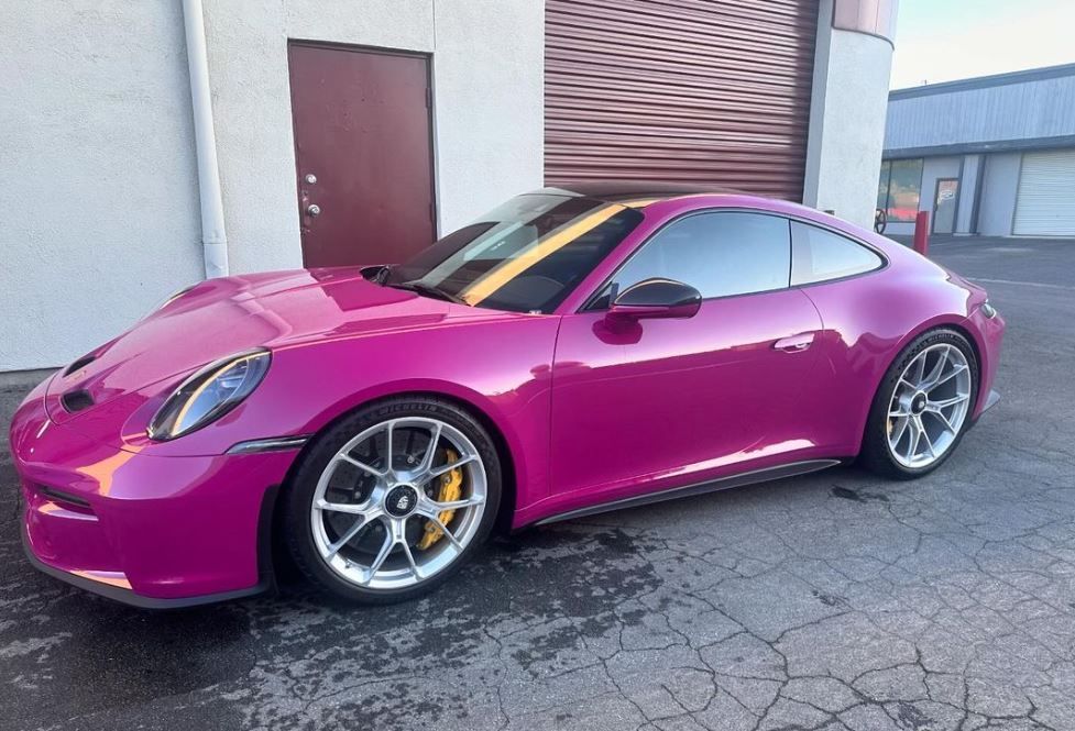 A pink Porsche 911 is parked in front of a building.