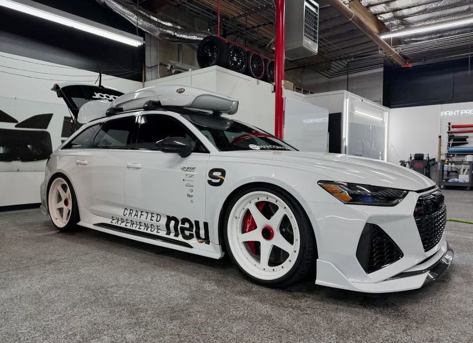 A white car with a roof rack is parked in a garage.