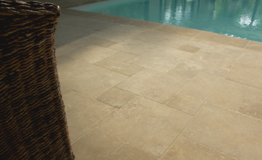 A wicker chair is sitting next to a tiled floor next to a swimming pool.