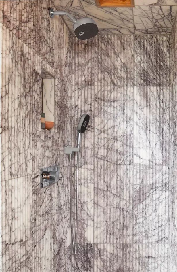 A shower with a marble wall and a shower head