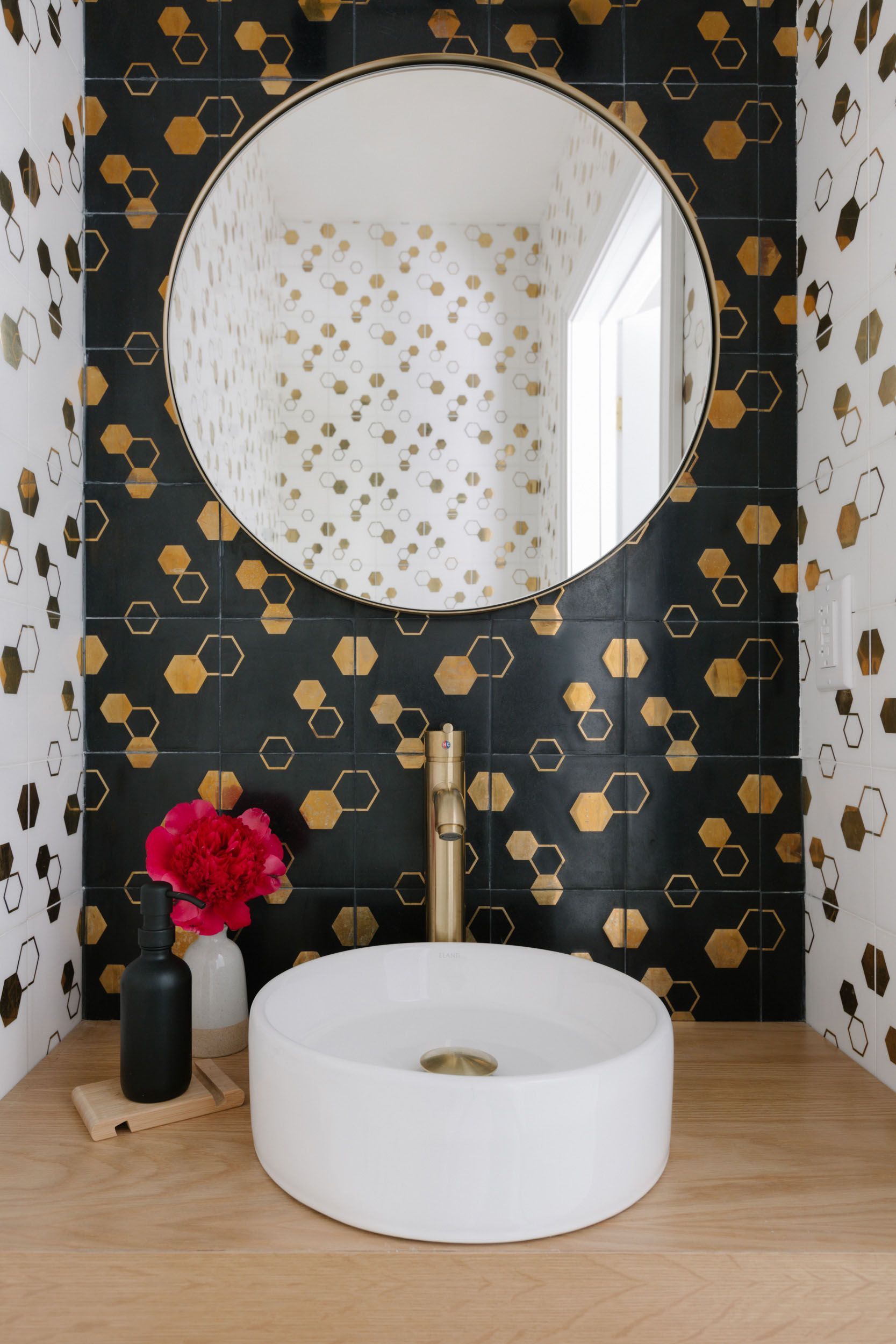 A bathroom with a sink, mirror, and black and gold tiles