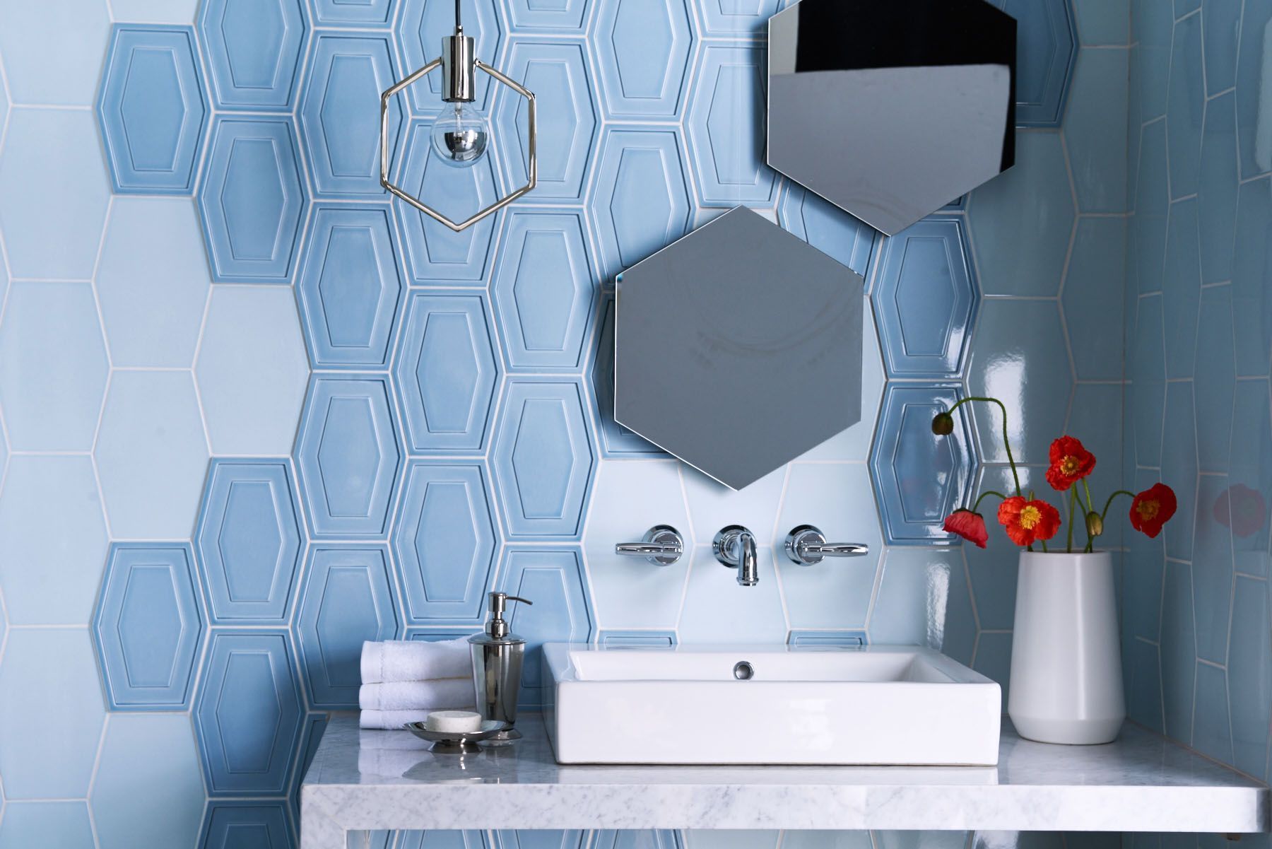 A bathroom with blue tiles, a sink, a mirror, and a vase of flowers