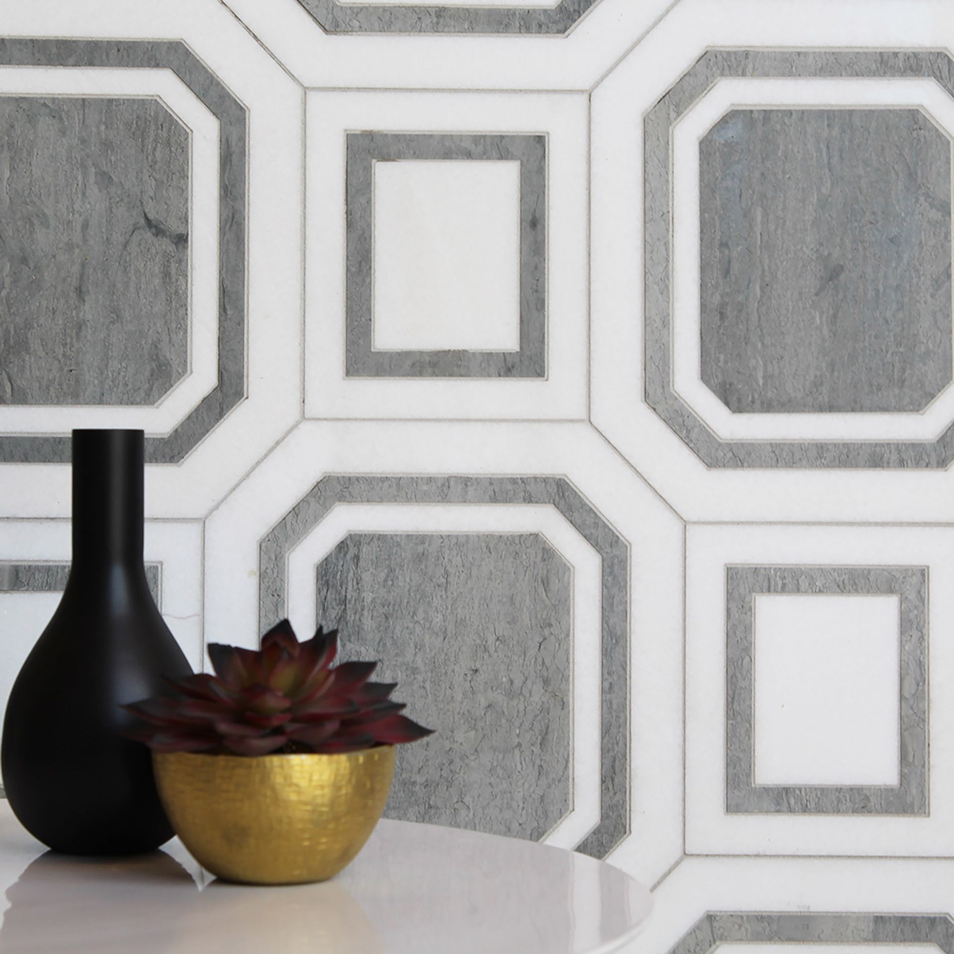 A black vase sits next to a gold potted plant