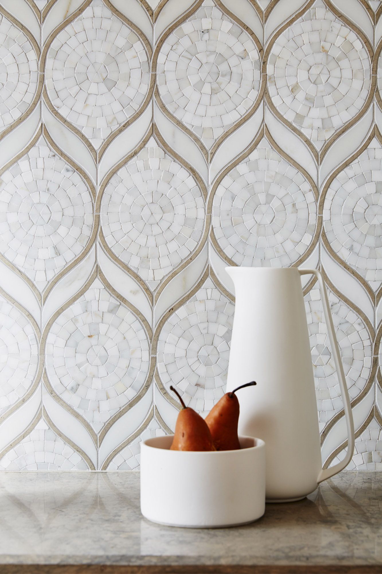 A bowl of pears sits on a counter next to a pitcher