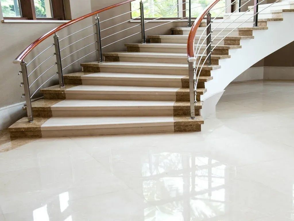 A curved staircase with a stainless steel railing and a white marble floor