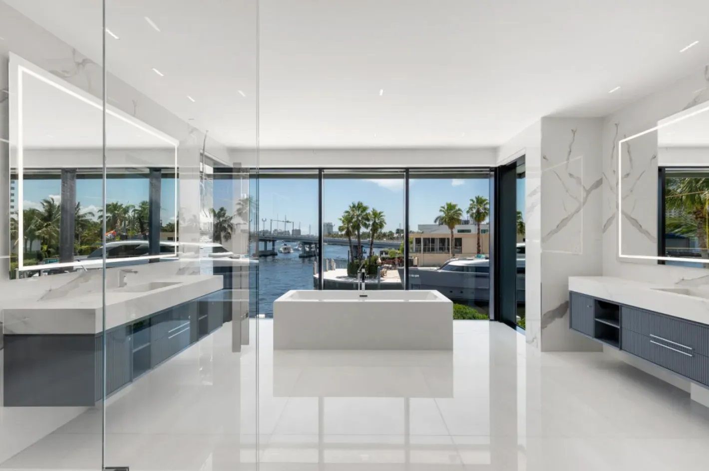 A bathroom with white marble flooring from Vietnam, a tub, sinks, mirrors and a large window