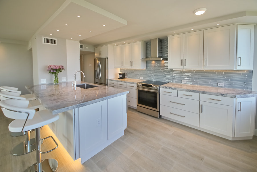 A kitchen with white cabinets , granite counter tops , stainless steel appliances and a large island.
