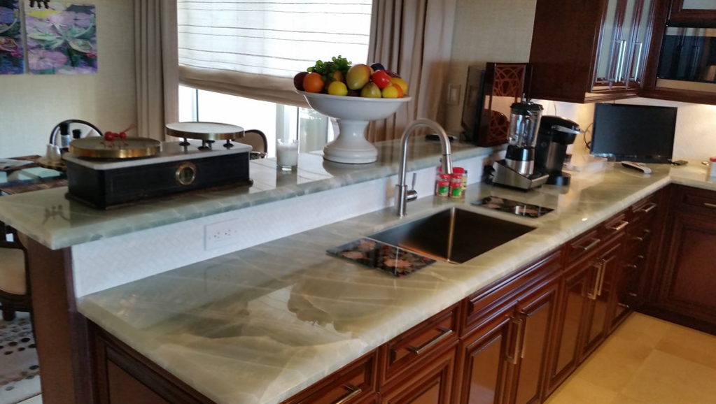 A kitchen with a sink , stove and a bowl of fruit on the counter.