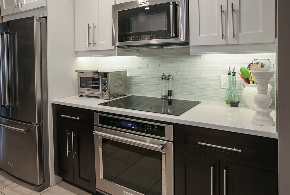 A kitchen with stainless steel appliances , black cabinets , a sink , microwave , refrigerator and toaster oven