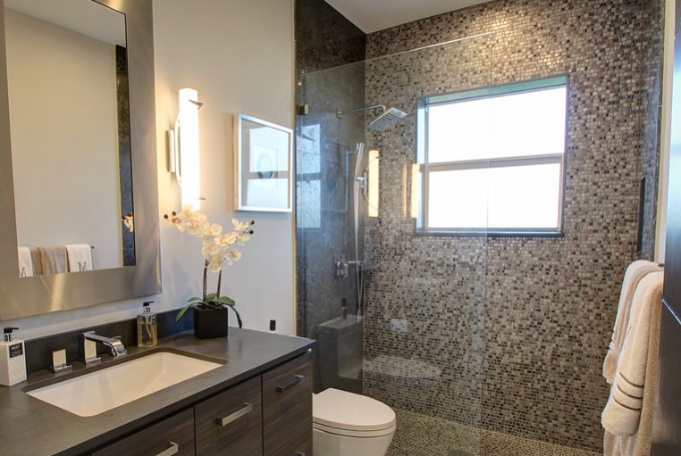 A bathroom with a toilet , sink , mirror and walk in shower.