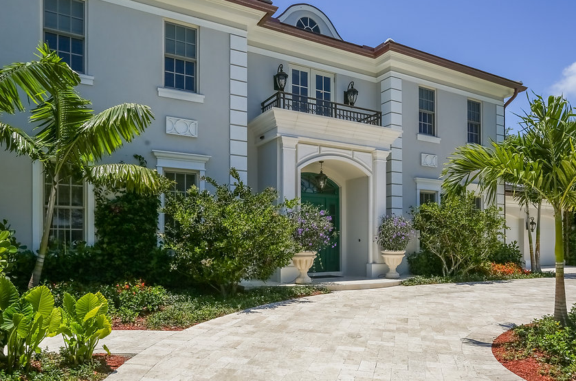 A large white house with a green door is surrounded by trees and bushes.