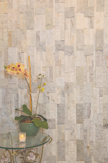 A vase of flowers is sitting on a glass table in front of a tiled wall.