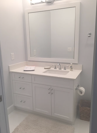 A bathroom with white cabinets , a sink , a mirror and a rug.