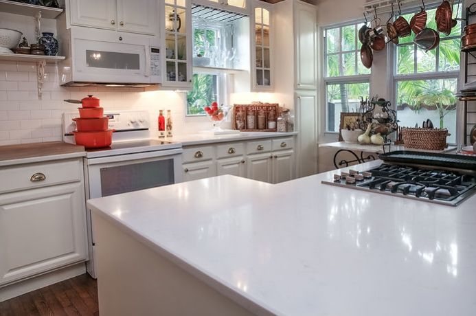 A kitchen with white cabinets , a stove , a microwave , and a large island.