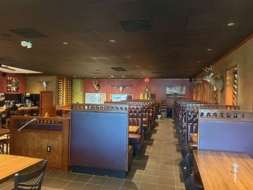 Empty restaurant dining area with booths, wooden tables, and warm brown-orange walls