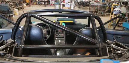 Black roll cage installed in a car interior. The car is in a workshop setting.