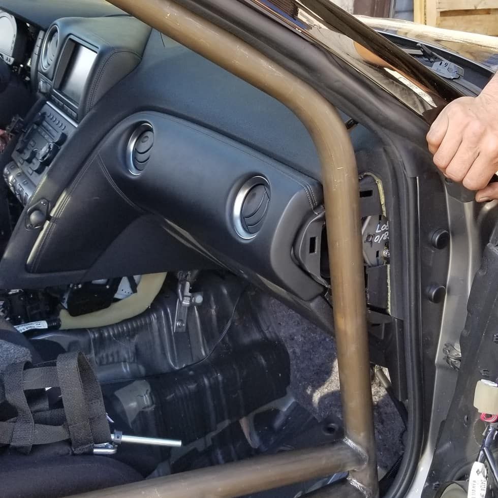 A car interior with a roll cage installed, dashboard visible, a person's hand opening the door.