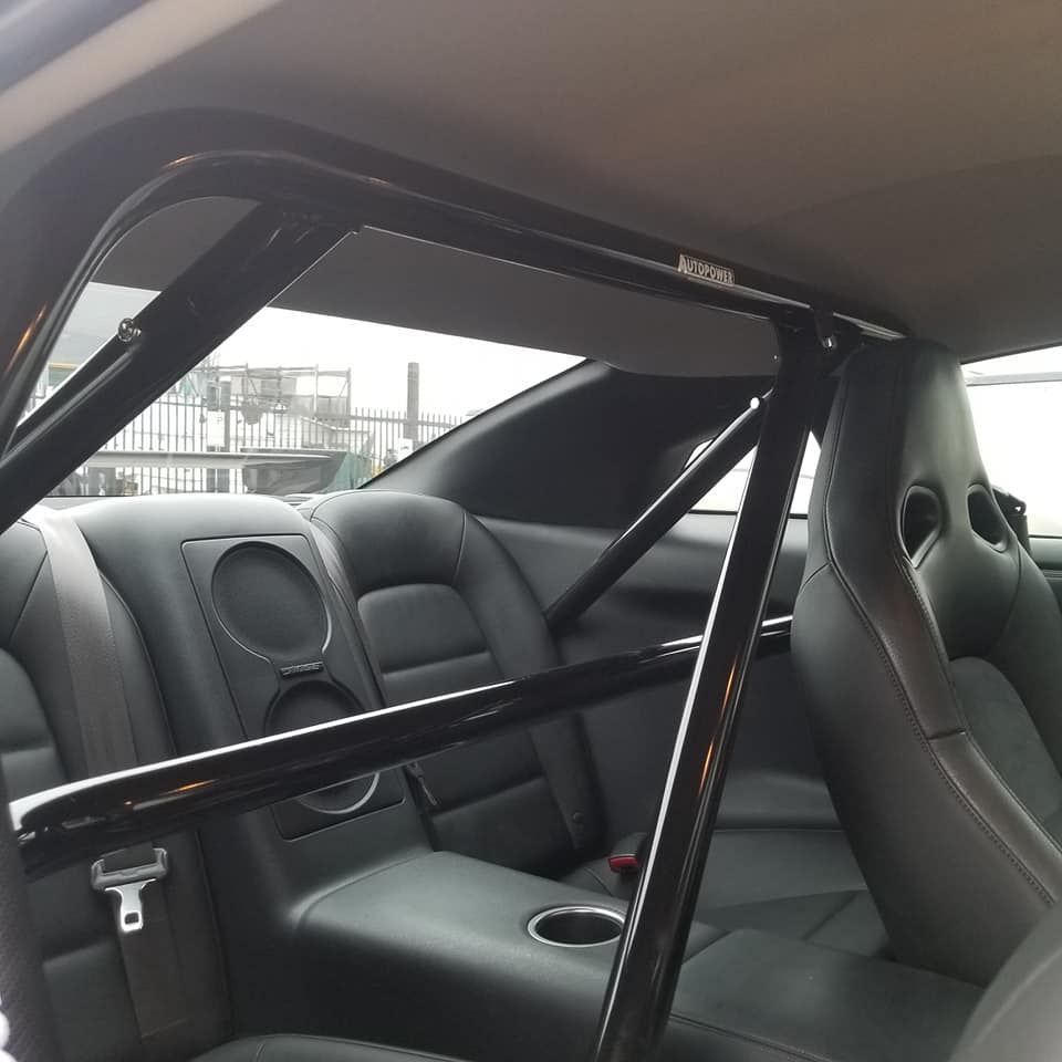 Black roll cage installed inside a car's rear passenger area, alongside black leather seats and cup holders.