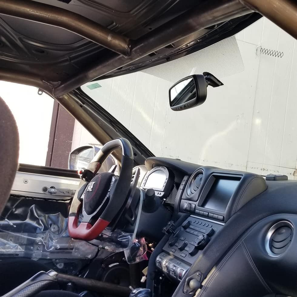 Interior of a race car, with roll cage, steering wheel, dashboard, and rearview mirror.