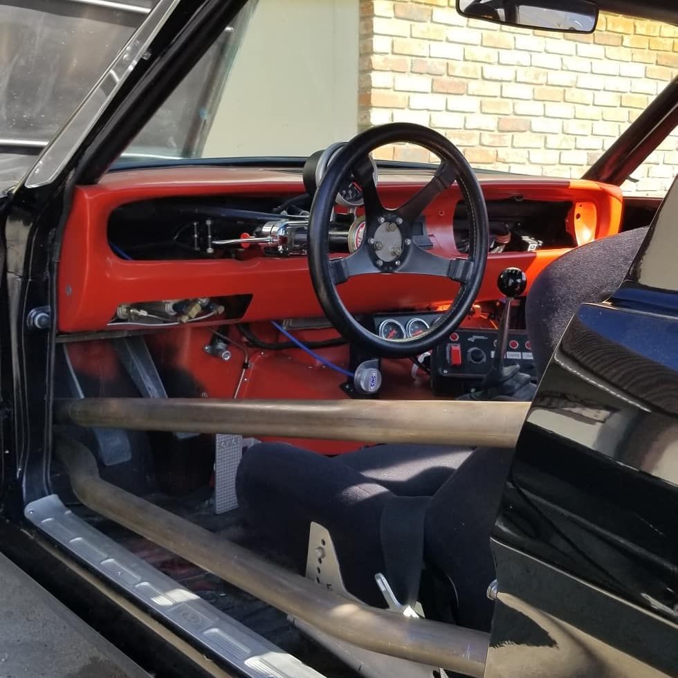 Black car interior with a roll cage, racing seat, orange dashboard, and black steering wheel.