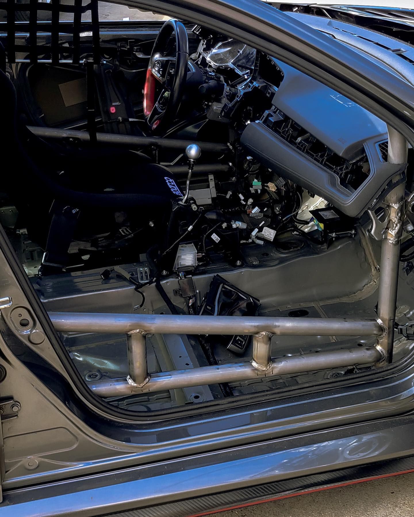 Interior view of a race car. The door frame is modified with roll cage tubing. Dashboard and other components are removed.