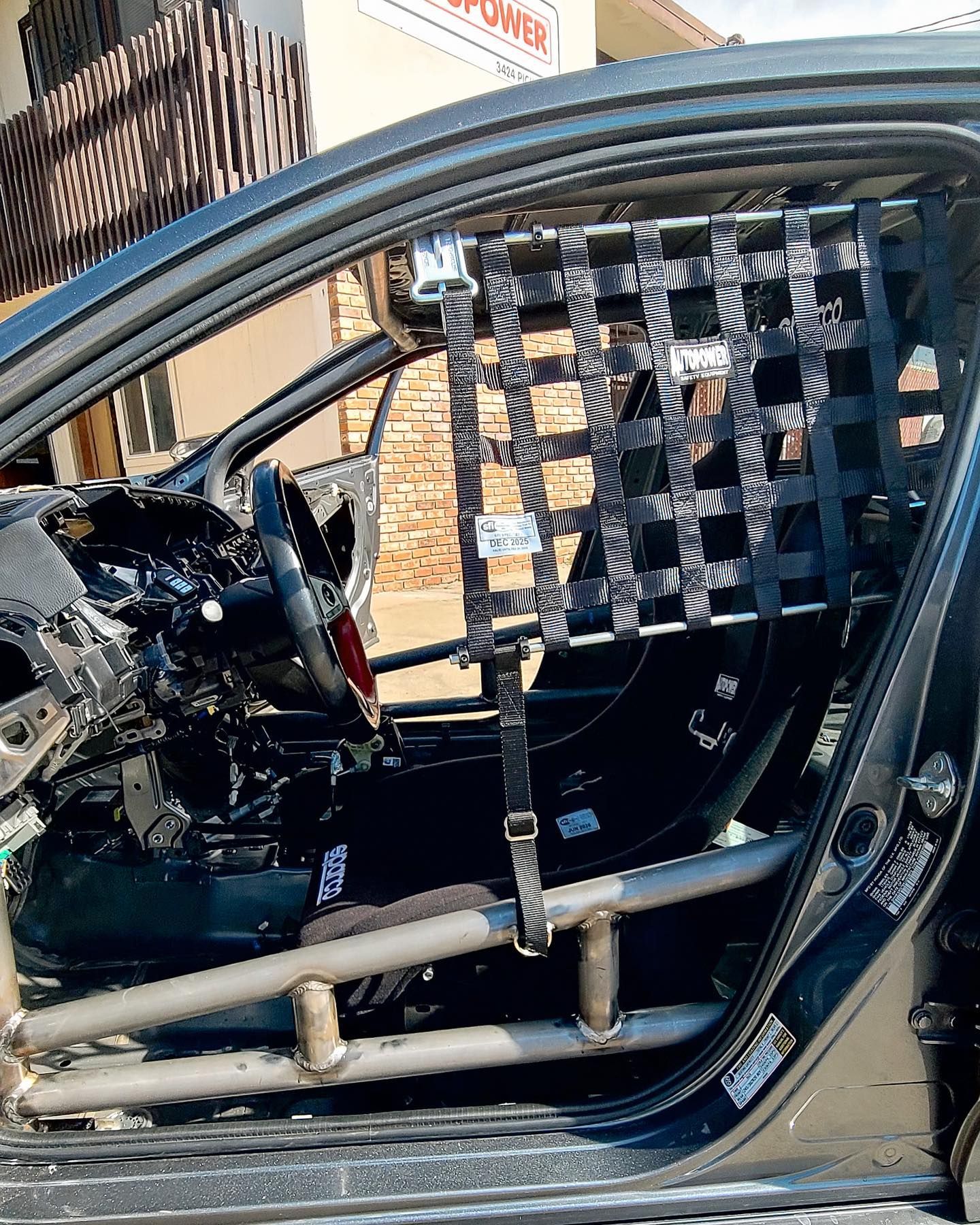 Race car interior with roll cage, safety net, racing seat, and steering wheel.