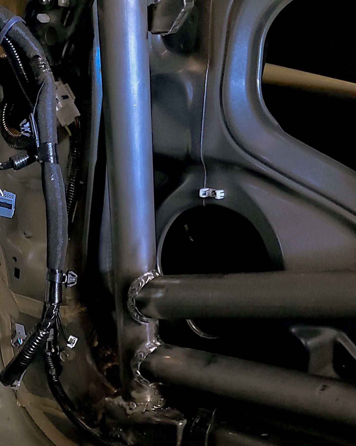 Interior car detail with welded steel roll cage. Dark grey metal against dark surroundings.