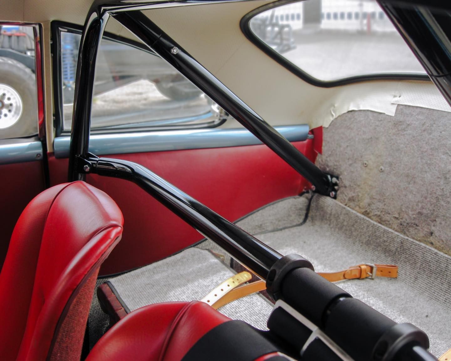 Interior of a red-seated classic car with a black roll cage installed.