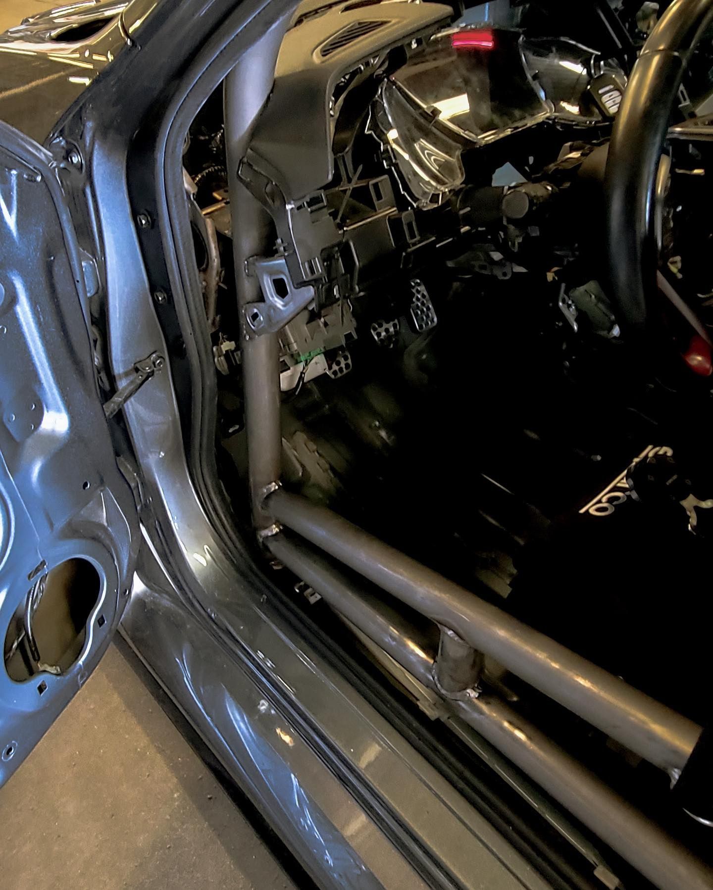 Interior view of a car with a roll cage installed, showing door frame, dashboard and footwell.