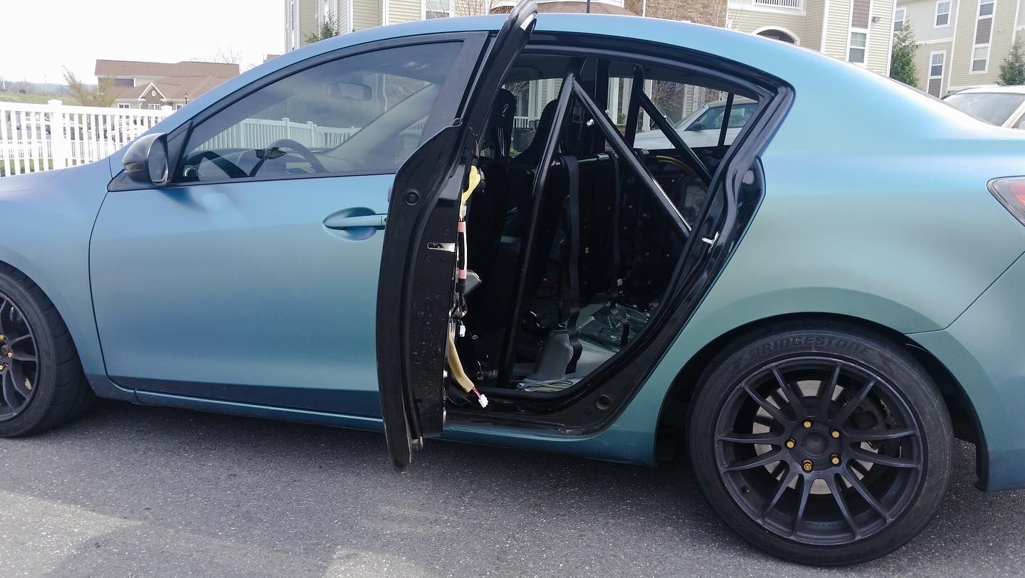 Blue car with open door revealing a roll cage. Dark rims, exterior paint gradient. Parked outdoors.