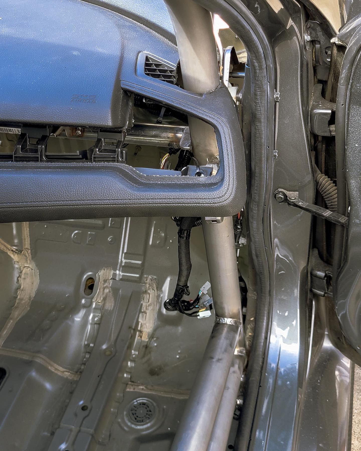 Gray car interior with roll cage bars and removed dashboard.