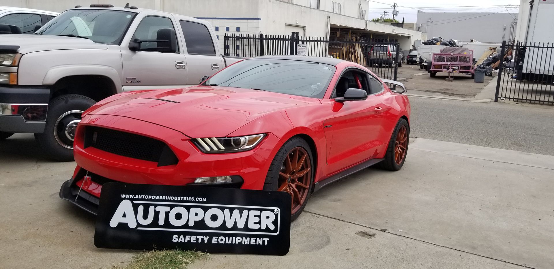 A red Ford Mustang sports car parked in front of a metal sign that says 