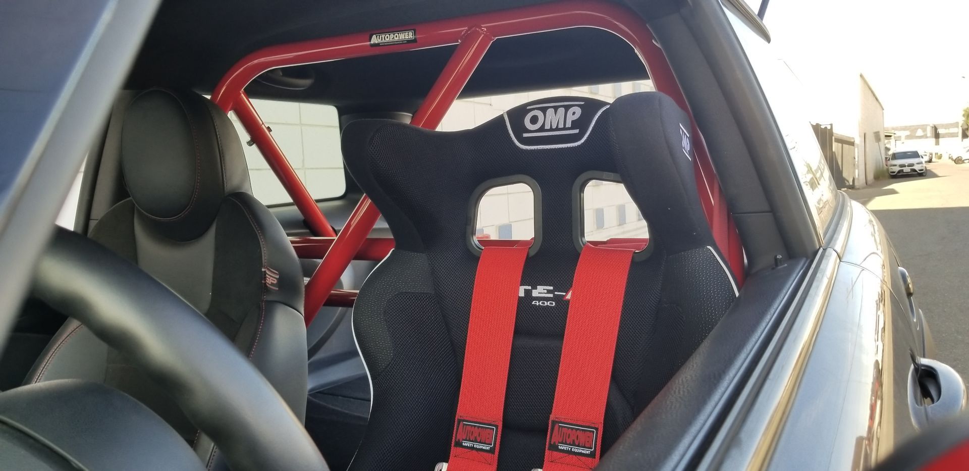 Interior of a black car with a red roll cage and a racing seat with red harness straps.