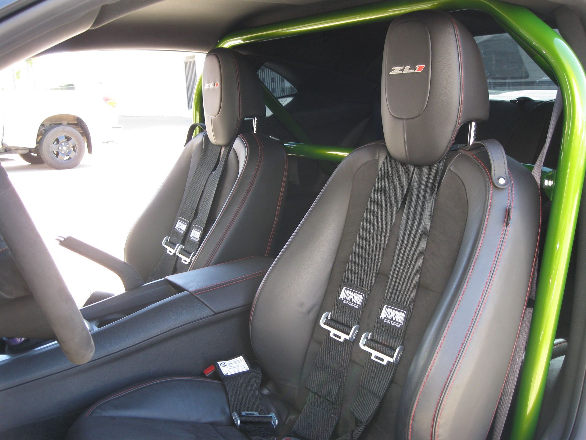Interior car shot: Black seats with racing harnesses, green roll cage, and 