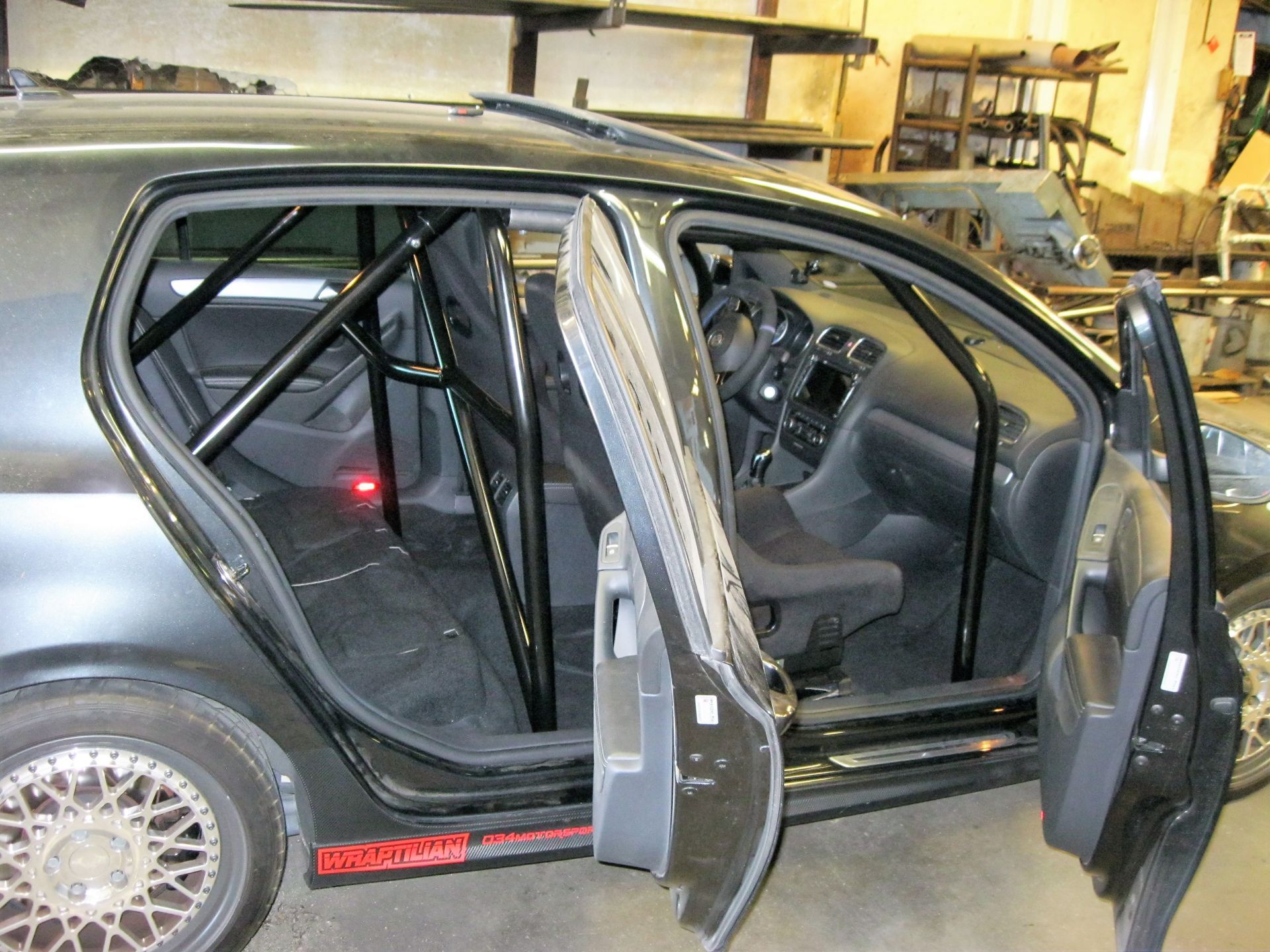 Black car interior with installed roll cage, doors open.